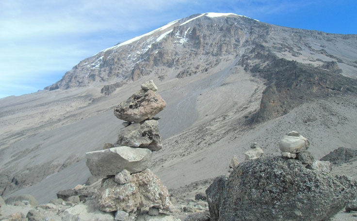 Snow-covered peak of Mount Kilimanjaro in clear weather and with stacked stones in front