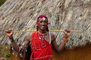 Maasai warrior holding his stick in front of a hut